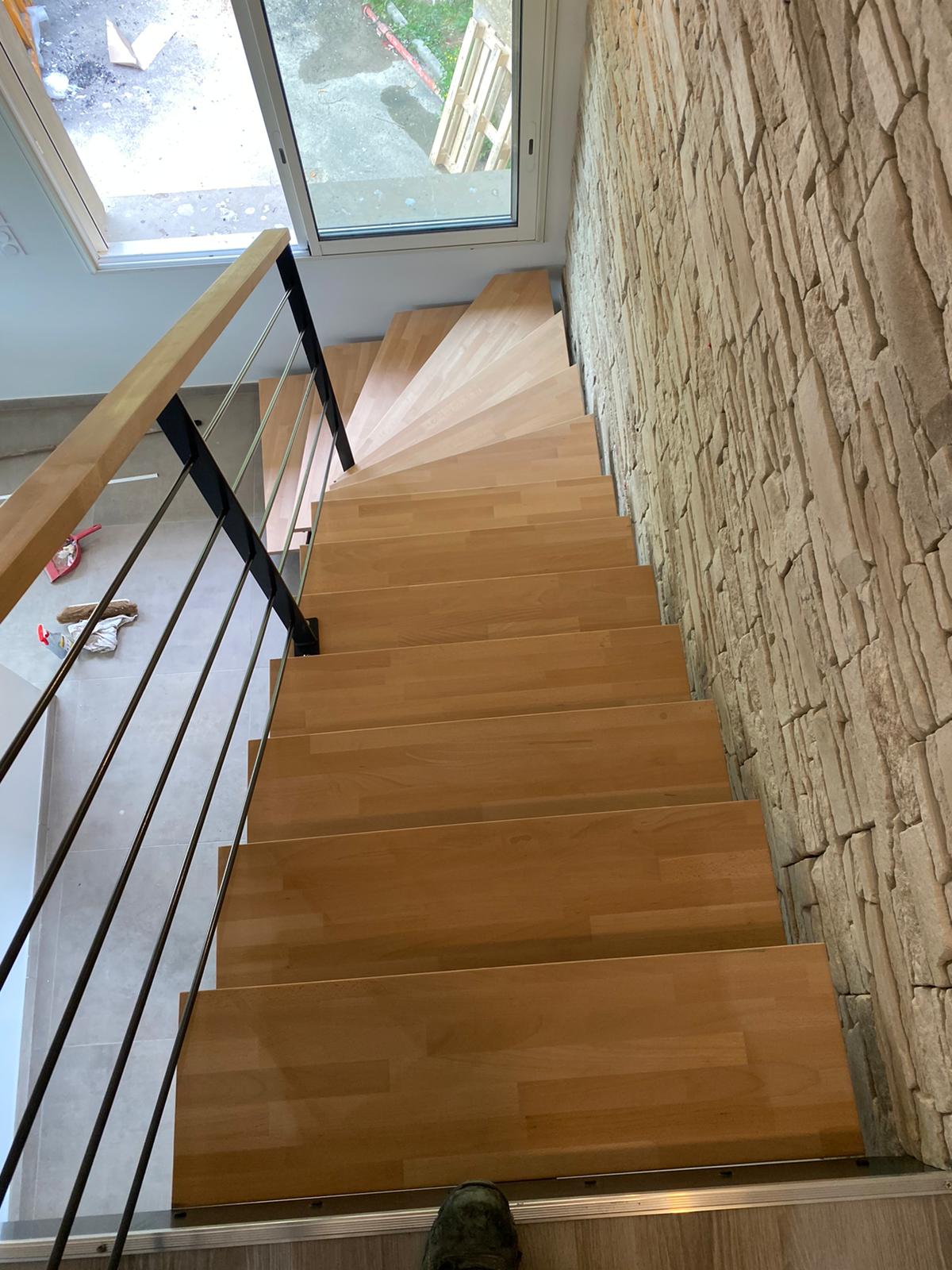 Vue depuis le palier des marches en bois et du tournant de l’escalier, avec sa rampe sombre.