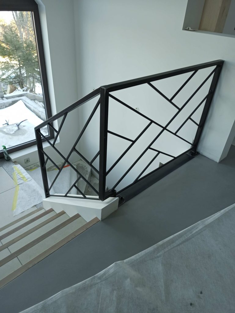 Vue de côté du garde-corps au tournant de l’escalier, avec remplissage géométrique en acier.