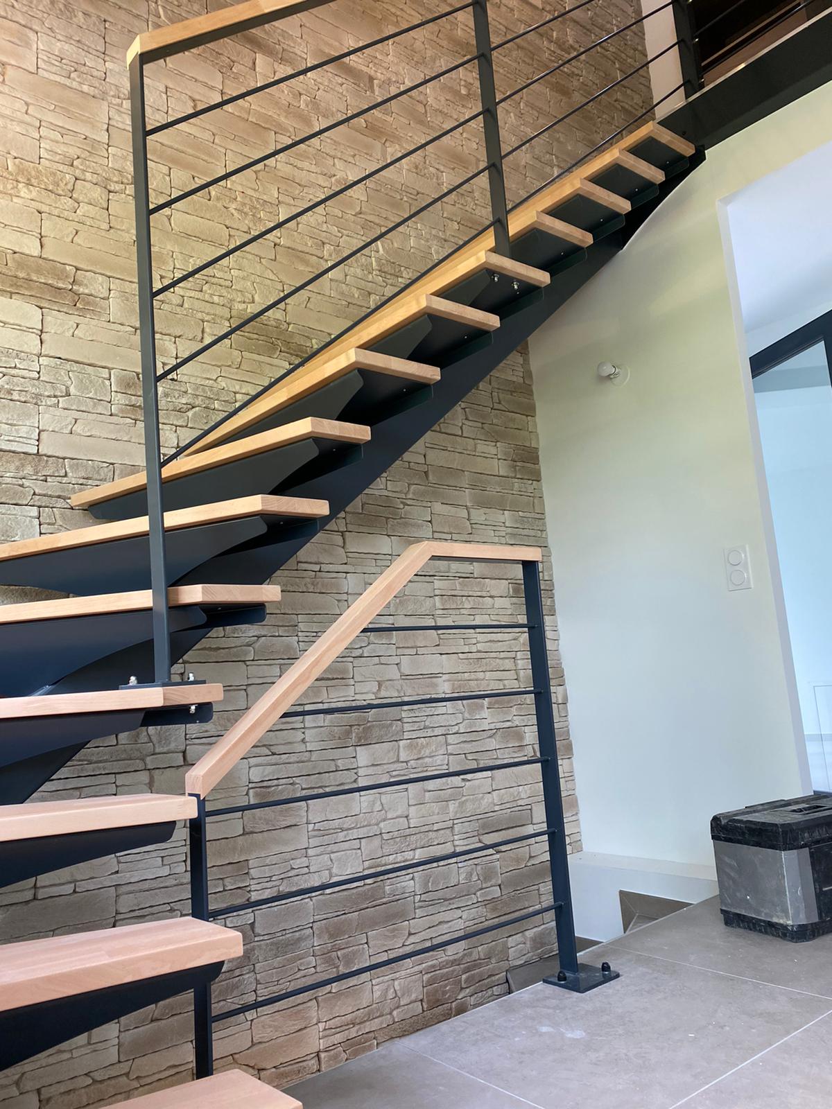 Vue latérale de l’escalier en acier noir et bois, avec le garde-corps du niveau inférieur.
