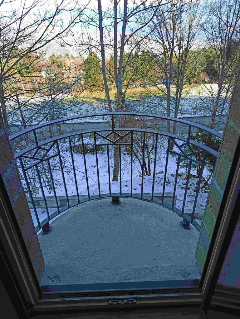 Garde-corps cintré du balcon vu depuis la porte, avec barreaux verticaux et motifs en partie haute.