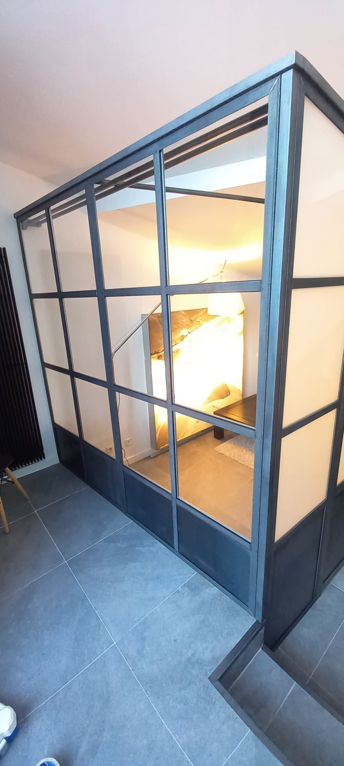 Retour vitré clair de la verrière, avec vue sur la chambre et sa lampe.