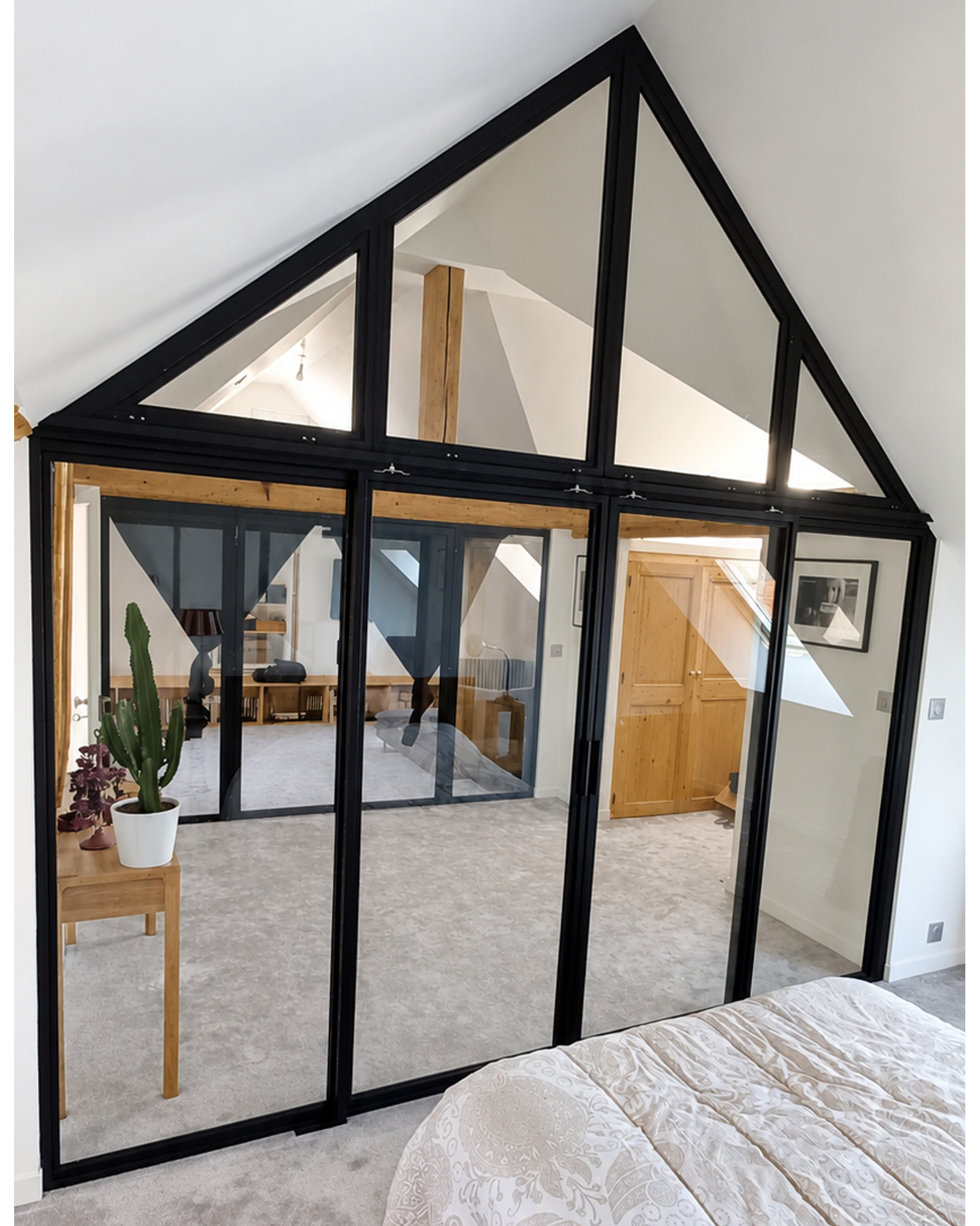 Verrière en acier noir vue depuis la chambre, avec les deux portes coulissantes fermées et l’imposte triangulaire.